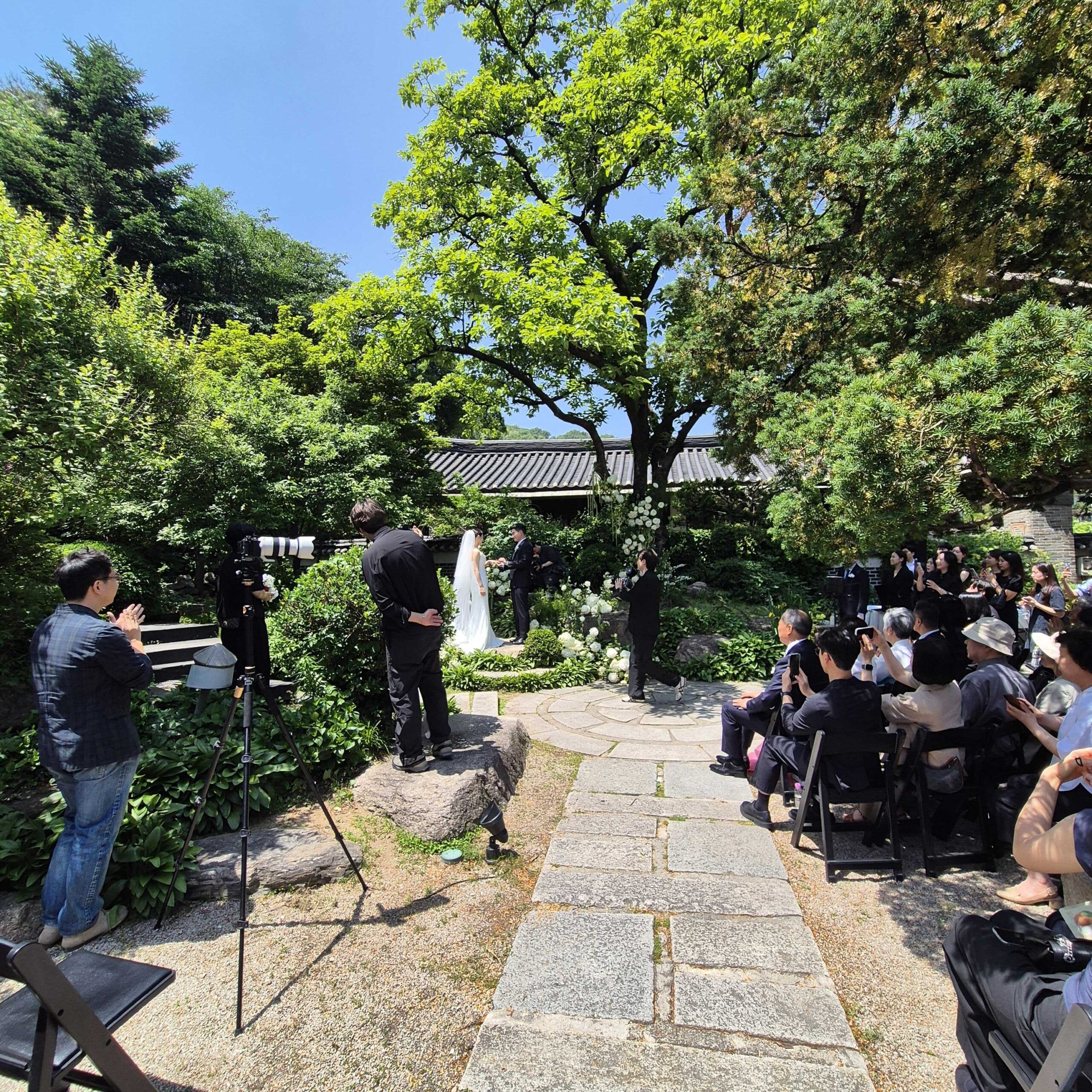 Outdoor Korean wedding ceremony in traditional garden with stone pathway and hanok roof Seoul