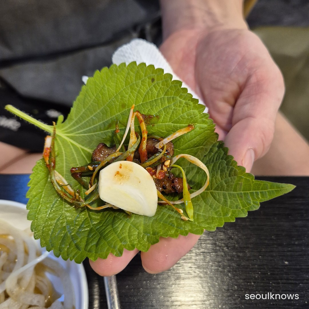 Hand holding a perilla leaf ssam wrap with meat and garlic