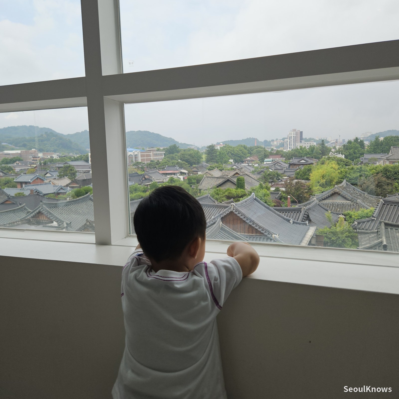 A child looking out at the hanok village from a window